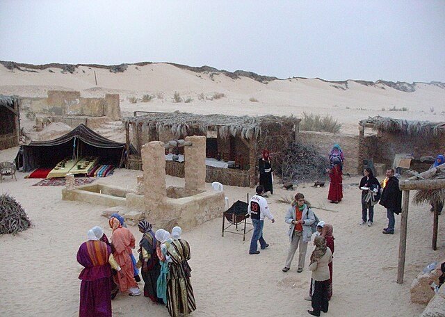فناء فيه بئر حجرية وخيمة بدوية، وزوار ونساء بالزي التقليدي